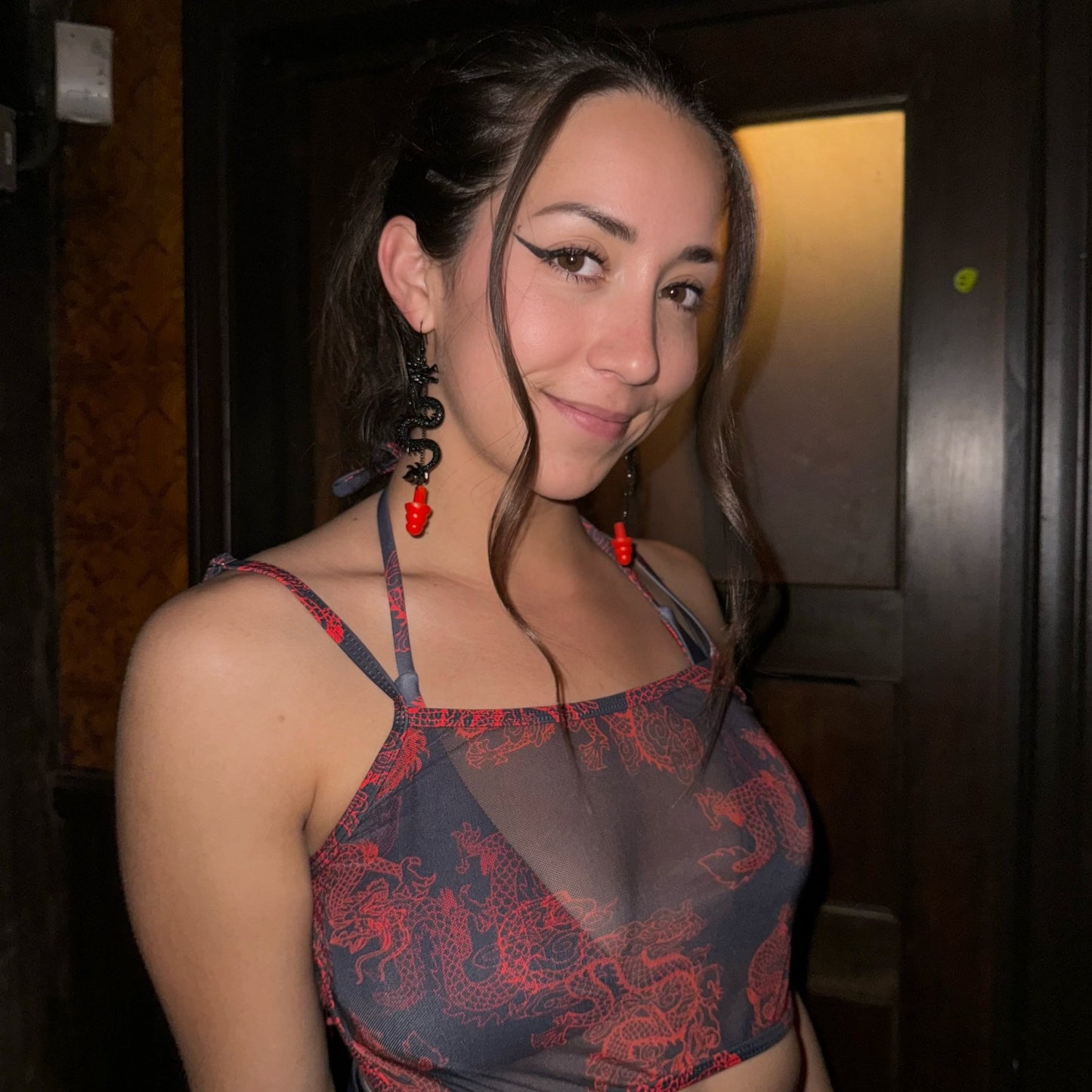Woman wearing sensory friendly earplug earrings with black dragons and red silicone ear plugs.