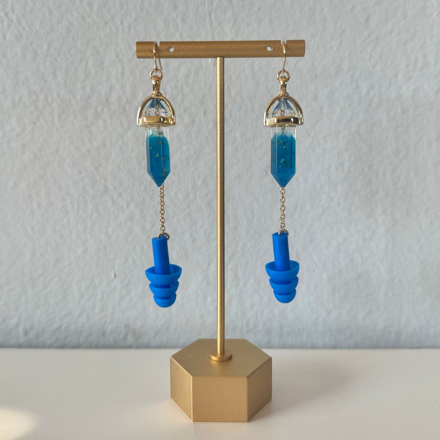 Deep blue crystal earplug earrings with a gold setting and chain. Trendy noise-reduction jewelry for ravers, festival-goers, and EDM lovers.