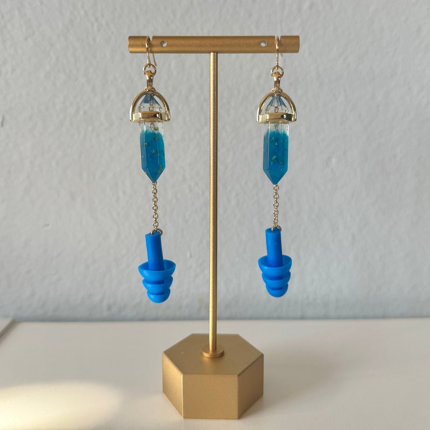 Stylish earplug earrings featuring deep blue crystals, matching blue ear plugs, and gold chain accents. Combines hearing protection with rave-ready fashion.