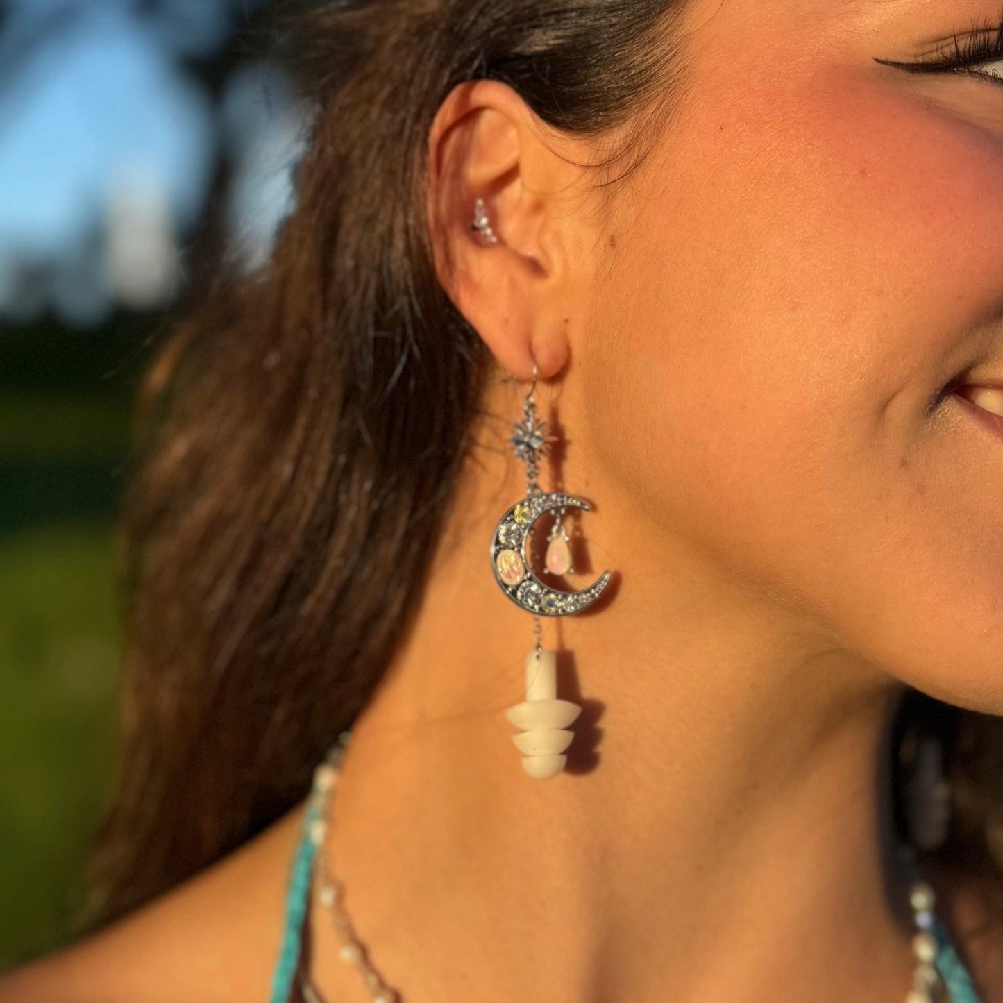 Beautiful woman wearing earplug earring jewelry with crystal encrusted moons and white ear plugs attached. Zoomed in view of earrings.