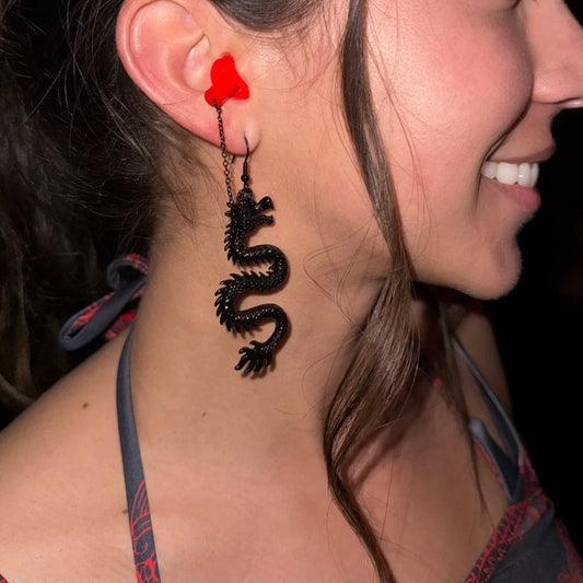 Woman wearing sensory friendly earplug earrings with black dragons and red silicone ear plugs. Zoomed in view.