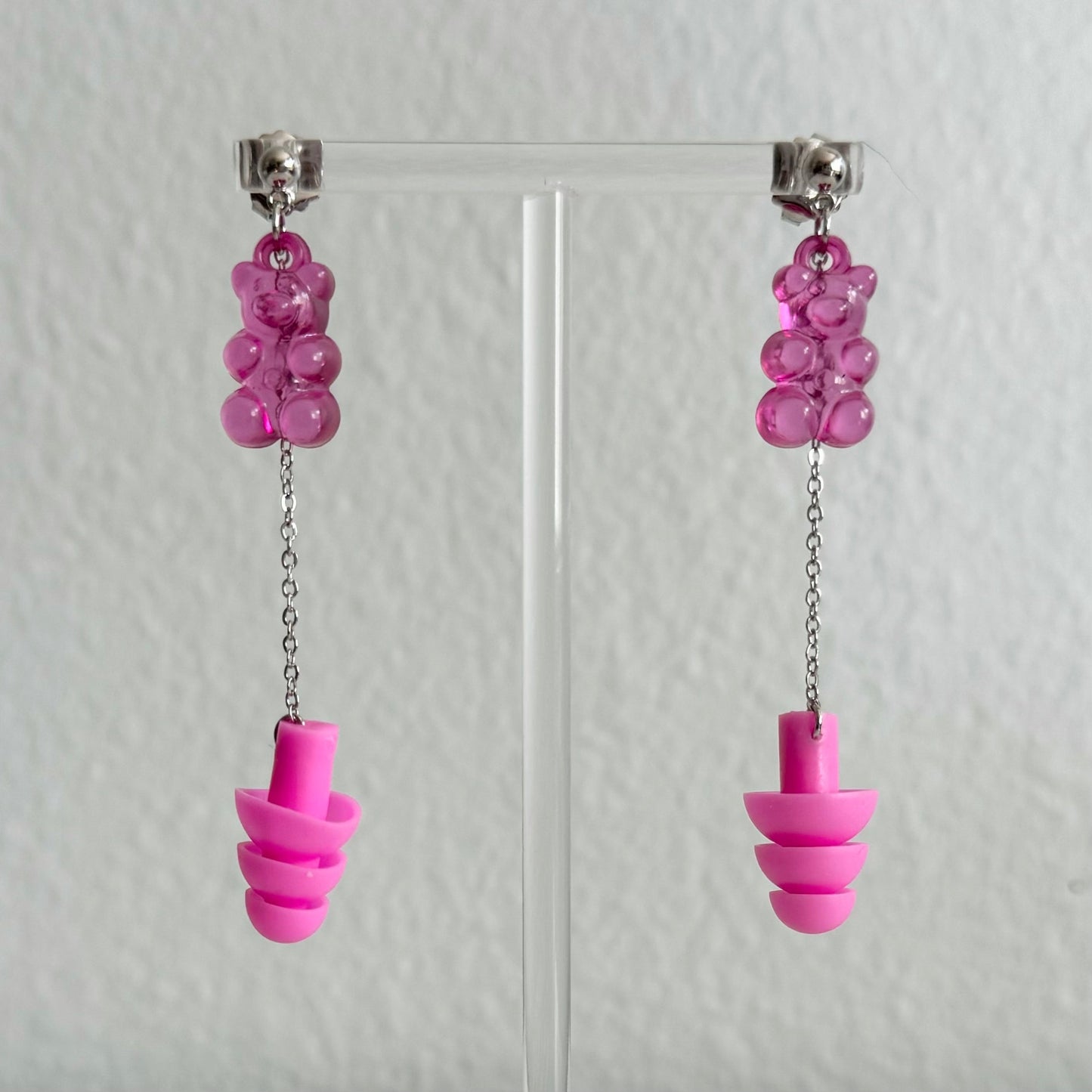 Neon pink gummy bear earplug earrings with pink ear plugs, silver chains, and a playful design. Stylish, functional jewelry makes a great gift for ravers and EDM fans.