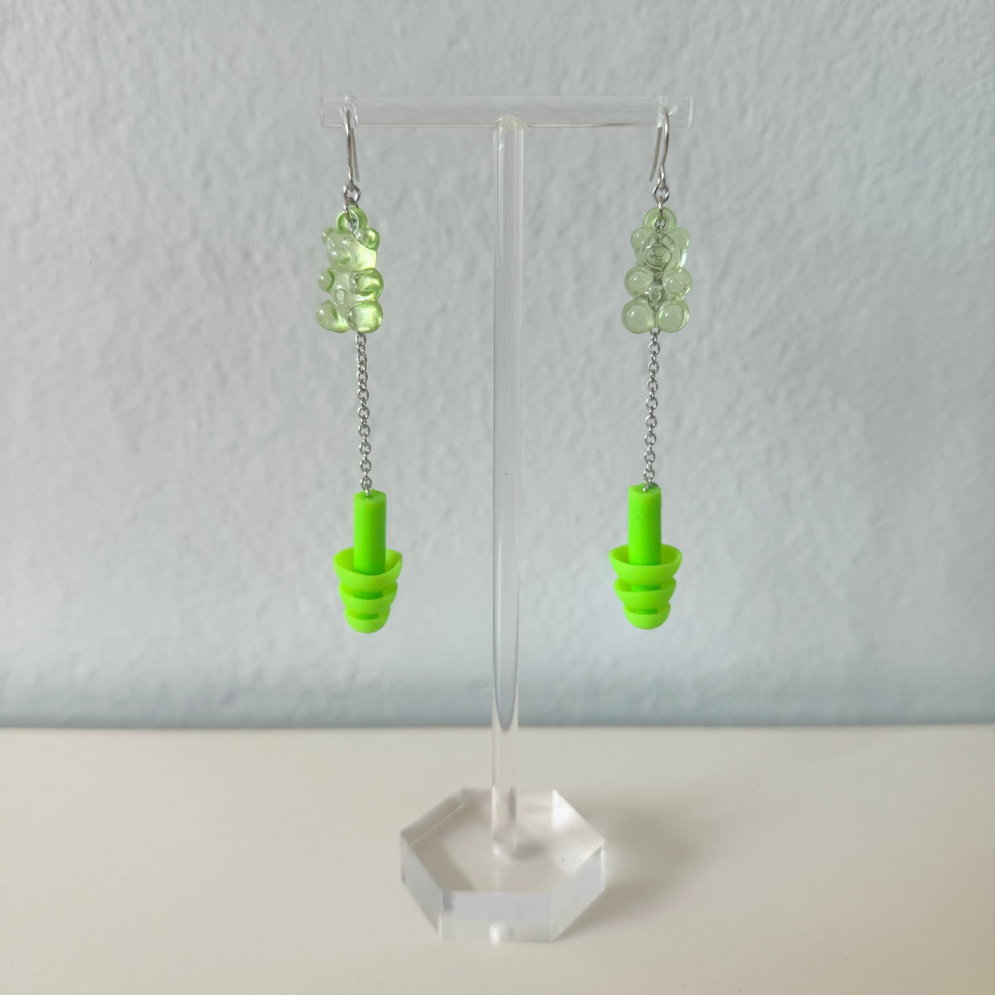 Green gummy bear earplug earrings with silver chains and green plugs, offering trendy hearing protection and a great gift for EDM lovers.