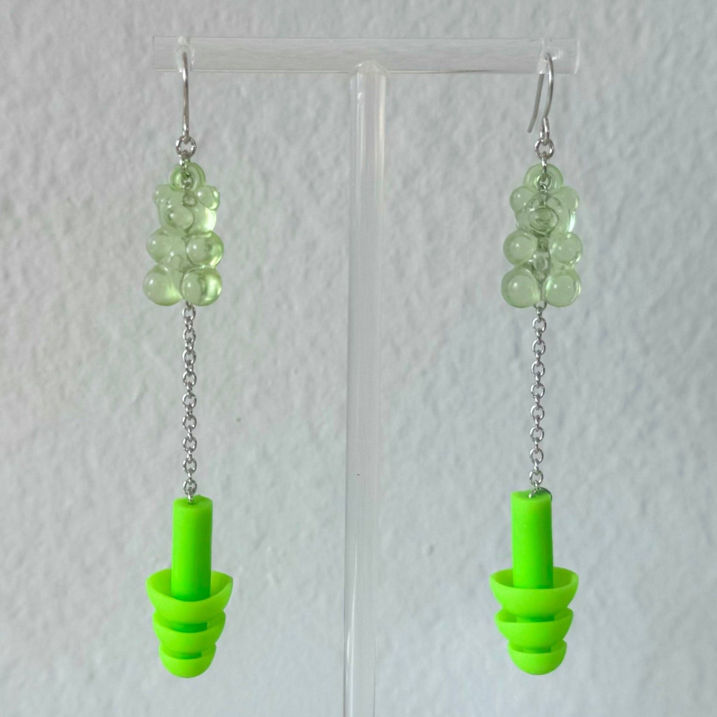 Green gummy bear earplug earrings with matching green ear plugs, silver chains, and setting, combining style and hearing protection. Ideal for ravers and EDM fans.