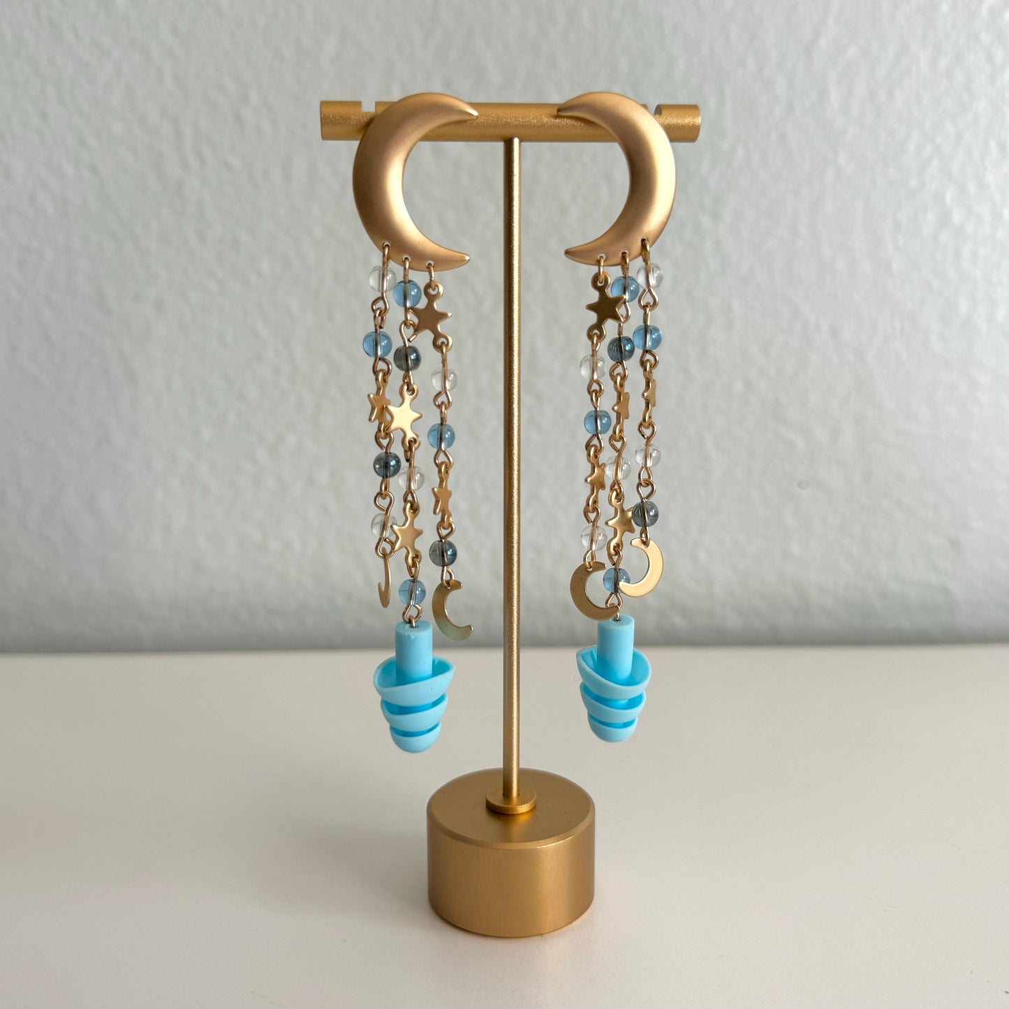 Gold moon Starry night chain drops on earring stand. Earplug earrings with blue beads, perfect gift for ravers seeking style and hearing protection. Sensory-friendly earrings with attached earplugs.