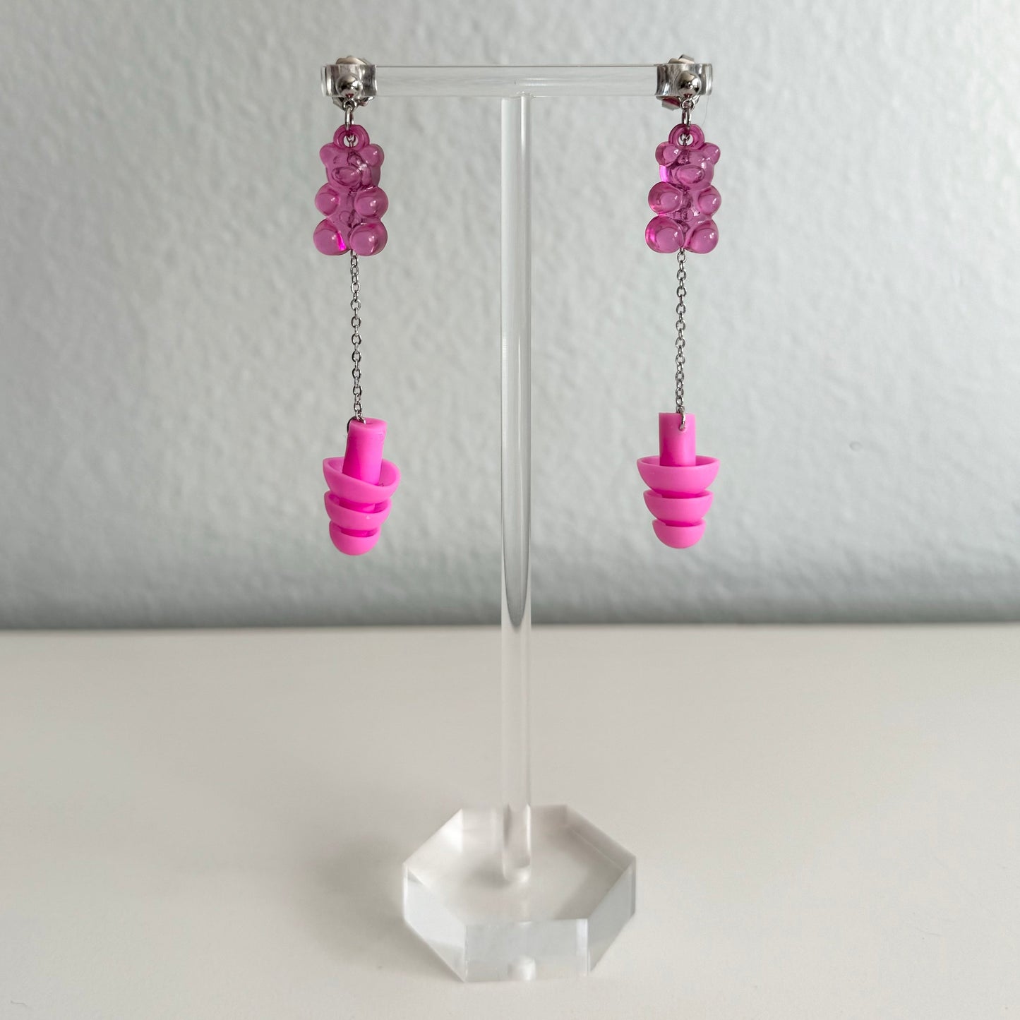 Neon pink gummy bear earplug earrings with pink earplugs, silver chains, and a playful design. Stylish, functional jewelry for ravers and EDM fans.