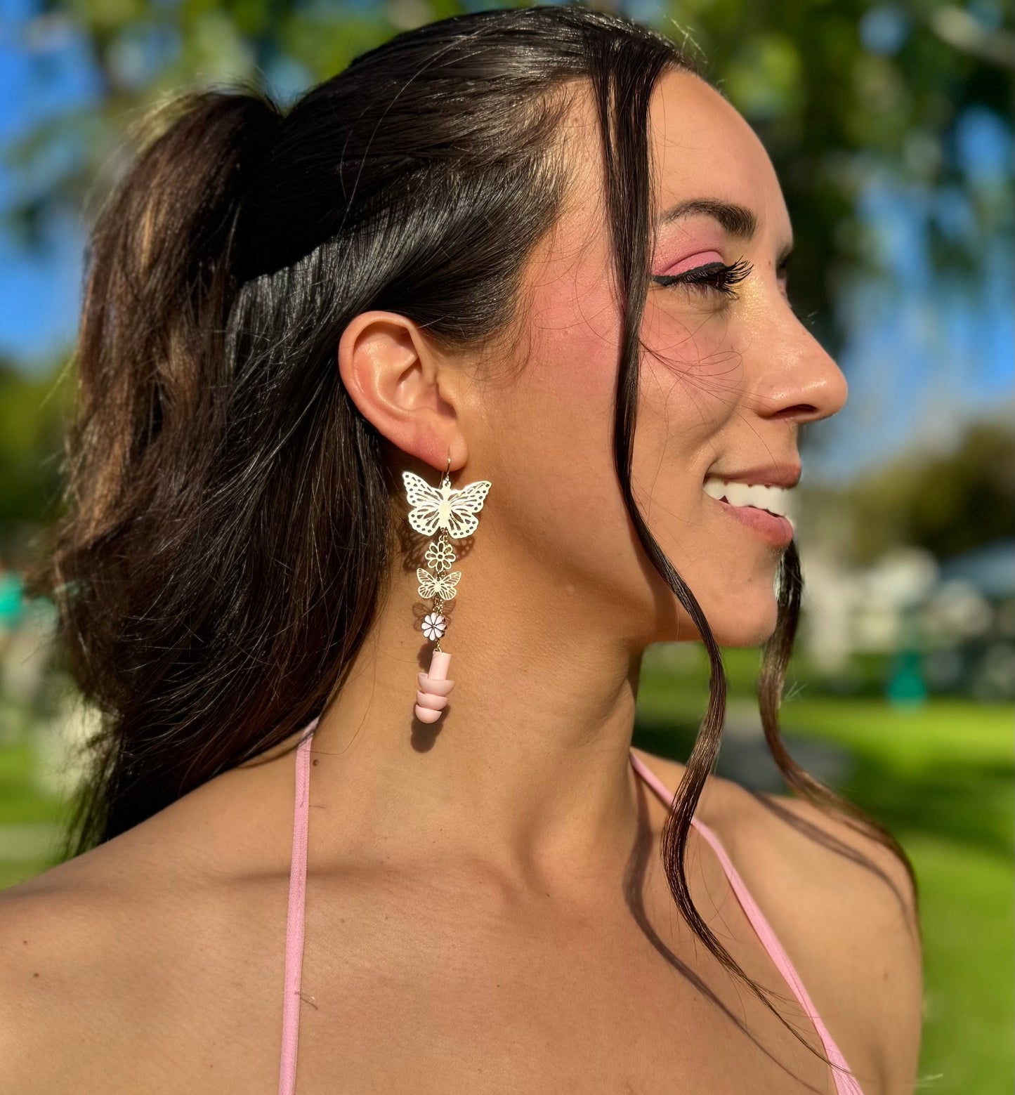 Beautiful woman wearing Pink Blossom Butterfly Earplug Earrings featuring colorful butterfly and flower designs with matching attached pink ear plugs. A stylish and functional accessory for hearing protection.
