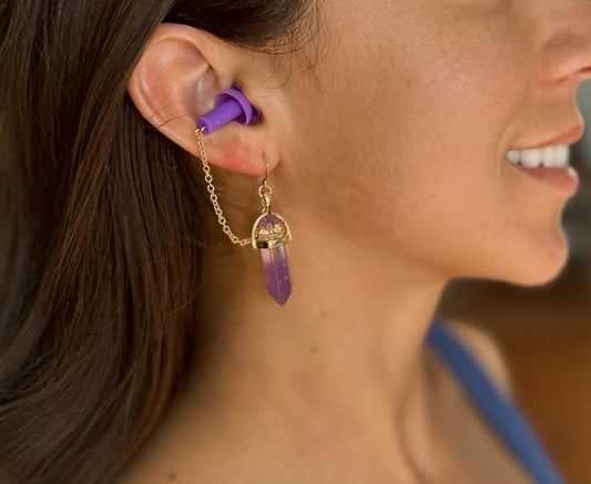 Woman wearing Purple Crystal Earplug earrings. Zoomed in view of the ear plugs. Stylish earplug earrings featuring deep purple crystals, matching purple earplugs, and gold chain accents. Combines hearing protection with rave-ready fashion.