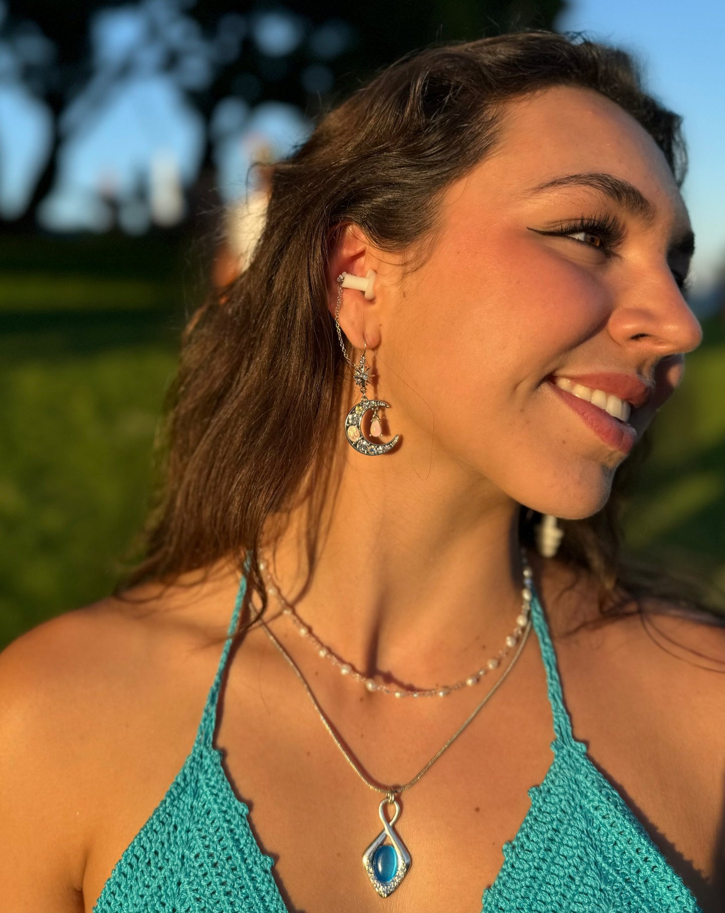 Beautiful woman wearing earplug earring jewelry with crystal encrusted moons and white ear plugs attached. Zoomed out view of earrings.
