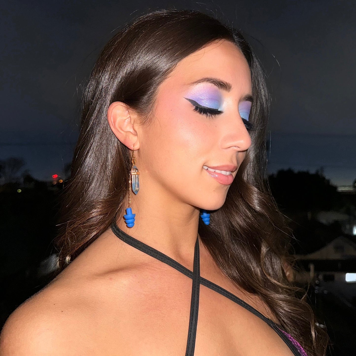 Woman wearing Elegant blue crystal earplug earrings with gold chains and matching earplugs. A fashionable accessory offering noise reduction for ravers and EDM fans.
