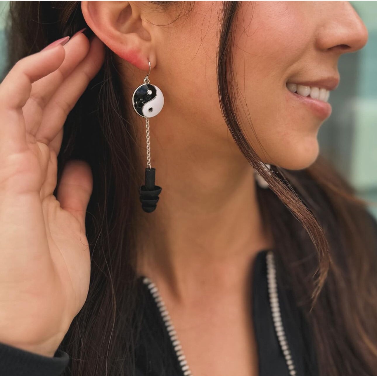 Woman wearing Yin and Yang earplug earrings with black and white silicone ear plugs attached. Sensory friendly jewelry for raves and concerts.