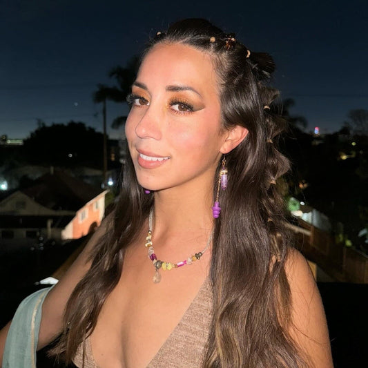 Woman wearing Purple Crystal Earplug  earrings - zoomed out view. Deep purple crystal earplug earrings with a gold setting and chain. Trendy noise-reduction jewelry for ravers, festival-goers, and EDM lovers.